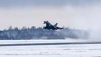 Mit feuerrot leuchtendem Nachbrenner hebt ein deutscher Eurofighter von der winterlichen Ämari Air Base in Estland ab.