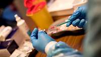 Hände in blauen Handschuhen ziehen eine Spritze auf