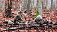 Zwei Soldaten liegen im Laubwald am Boden und haben ihren Waffen im Anschlag.