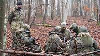 Ein Gruppe Soldaten hockt im Wald, ein Soldat in der Mitte erklärt etwas.