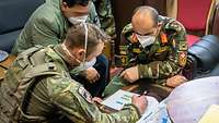 Zwei Soldaten und ein Zivilist sitzen an einem Tisch und blicken gemeinsam auf ein Dokument
