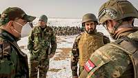 Vier Soldaten stehen im Vordergrund im Kreis, im Hintergrund sitzen afghanische Soldaten