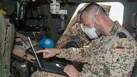 Ein Soldat zeigt einem weiteren Soldaten in einem Gefechtsfahrzeug etwas auf dem Bildschirm eines Laptops