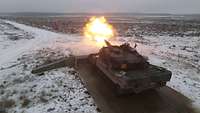 Der Kampfpanzer Leopard 2A6 feuert aus seiner schneebedeckten Stellung, am Rohr eine meterlange Flamme 