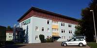 Ein hellgrüner, länglicher, moderner Plattenbau. Davor steht ein Auto.