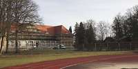 Ein zweistöckiges, längliches Gebäude mit Gauben, großen Fenstern und einem roten Ziegeldach
