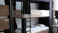 Ein modernes Doppelstockbett mit schwarzer Metallleiter und Holzfurnier verkleidet