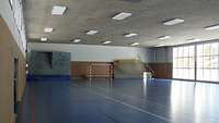 Blick in eine Turnhalle mit blauem Boden und großen Fenstern