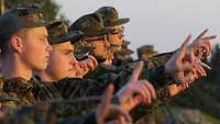 Soldaten stehen in einer Reihe und strecken einen Arm und den Zeigefinger nach vorn.