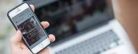 www.bmvg.de Die Website www.bmvg.de in einem Smartphone, im Hintergrund ein Notebook.