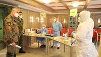 Zwei Personen in Uniform lassen sich von drei Personen in Vollschutz in den Ablauf der Abstrichentnahme einweisen