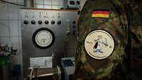 Ein Soldat mit einem Verbandsabzeichen auf dem Ärmel seiner Feldbluse steht vor Teilen des mobilen Labors der Fachgruppe.