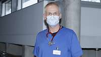 Ein Arzt in blauer Krankenhauskleidung steht auf dem Flur eines Krankenhauses.