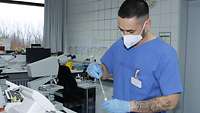 Ein Mann in Laborbekleidung entnimmt mit einer Pipette Flüssigkeit aus einem Röhrchen.