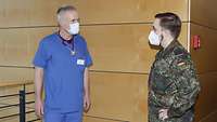 Ein Arzt in blauer Krankenhauskleidung und ein Soldat unterhalten sich in der Lobby des Krankenhauses.