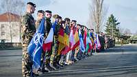 Soldaten verschiedener Länder stehen in Reihe und halten verschiedene Nationalflaggen. 