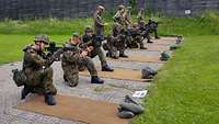 Mehrere Soldaten hocken nebeneinander und halten knieend aufgelegt ihre Waffen in eine Richtung.
