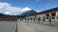 Soldaten in blauer Sportbekleidung laufen in einer Reihe hintereinander, im Hintergrund Berge.
