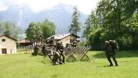 Mehrere Soldaten klettern mit Marschgepäck und Waffen durch ein rautenförmiges Holzgerüst.