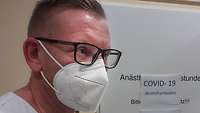Porträtaufnahme eines Mannes im weißer Arbeitskleidung, der Brille und eine Atemschutzmaske trägt