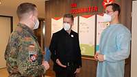 Soldat im Gespräch mit einem Zivilisten und einem Soldaten in medizinischer Schutzkleidung.