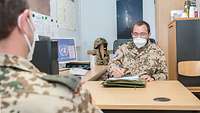 Zwei Soldaten sitzen sich in einem Büro am Tisch gegenüber 