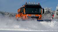 Ein orangefarbenes Winterdienst-Räumfahrzeug der Bundeswehr schiebt Schneeberge von einer Straße.
