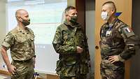 Ein deutscher Oberst weist einen französischen General in die Übung ein. Links steht ein englischer Soldat in Grundstellung.