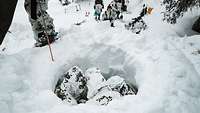 Vier Soldaten mit Schneetarnanzug stehen im Kreis in einem Schneeloch dicht beieinander. 
