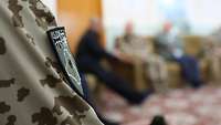 Im Vordergrund des Bildes ein Arm eines deutschen Soldaten in Uniform, auf seinem Patch ist eine Palme abgebildet 
