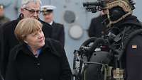 Eine Frau im dunkelblauen Wintermantel spricht mit einem Soldaten im Taucheranzug und mit Schutzhelm.