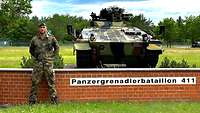 Ein Soldat mit grünem Barett steht vor einem Panzer, der auf einem gemauerten Sockel steht.