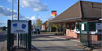 Rechts Blick auf ein Wachhaus mit großem Dach, davor zwei Fahrbahnen für die Ein- und Ausfahrt