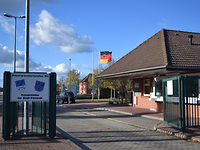 Wache Rechts Blick auf ein Wachhaus mit großem Dach, davor zwei Fahrbahnen für die Ein- und Ausfahrt