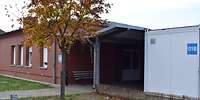 Flaches, rotes, Backsteingebäude mit einem Containeranbau und einem Baum davor