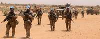 Bundeswehr soldiers with weapons and blue UN caps on patrol in a desert landscape