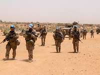 Bundeswehr soldiers with weapons and blue UN caps on patrol in a desert landscape