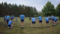 Mehrere Soldaten in blauer Sportkleidung stehen auf dem Rasen im Kreis und machen Aufwärmübungen.