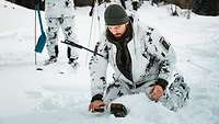 Ein Soldat in Schneetarnuniform fährt mit einem Lawinensuchgerät über den Schnee.
