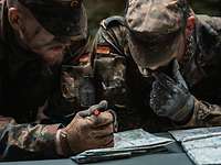 Soldaten in grüner Uniform schauen auf eine Faltkarte auf einem grauen Tisch.