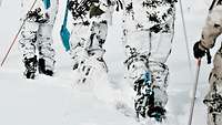Soldaten in Schneetarnuniform laufen auf Skiern und in Schneeschuhen durch den Schnee.