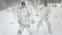 Soldaten in Schneetarnuniform auf Skiern werden an einer Leine über den Schnee gezogen.