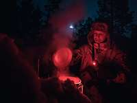 Ein Soldat schmilzt bei Dunkelheit und rotem Licht Schnee in einem Topf.