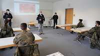 Ein Mann in einer DRK-Uniform steht mit zwei weiteren Männern vor einer Leinwand und begrüßt die Teilnehmer einer Schulung.