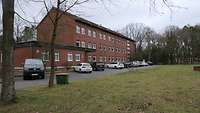 Unterkunftsgebäude Ein dreigeschossiges Gebäude mit Satteldach und Backsteinfassade, umgeben von Bäumen