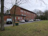 Ein dreigeschossiges Gebäude mit Satteldach und Backsteinfassade, umgeben von Bäumen