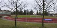 Um einen Rasen mit aufgestellten Fußballtoren verläuft oval eine rote breite Tartanbahn.