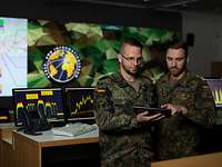 Soldaten im Network Operation Center in Rheinbach Zwei Soldaten stehen nebeneinander und schauen auf ein Tablet, hinter ihnen mehrere Computer und ein großes Wanddisplay