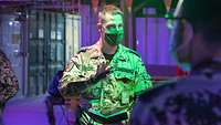 Ein deutscher Soldat steht abends im grünen Licht vor mehreren Soldaten und hält in der rechten Hand ein Notizbuch
