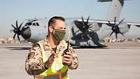 Ein Soldat mit einem Funkgerät steht vor einem grauen Flugzeug